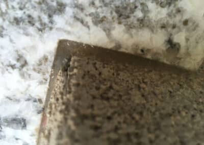 Close-up of a stone corner, featuring a rough-textured, light brown surface meeting a smooth, marbled white and gray slab. The image highlights the contrast between the materials and their textures.
