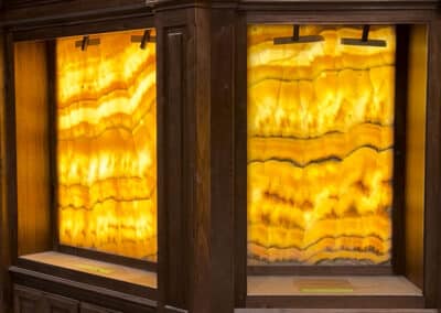 Two illuminated stone panels with amber and gold tones framed by dark wood. The panels have wavy patterns and are under small overhead lights, enhancing their warm glow.